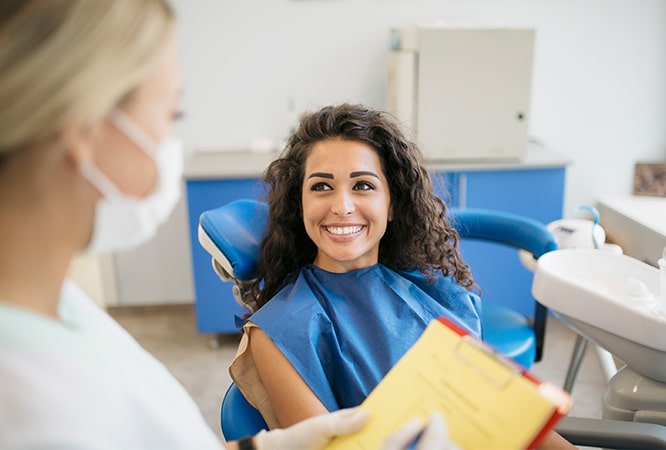 Dentist in blue uniform explains treatment to patient in dental office setting.